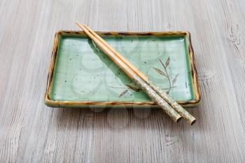 one green square plate with chopsticks on gray brown table