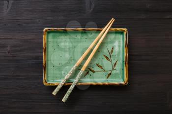 top view of one green square plate with chopsticks on dark brown table
