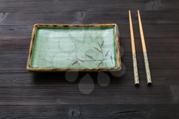 one green square plate and chopsticks on dark brown table