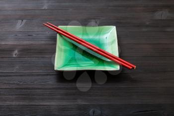 one green square saucer with red chopsticks on dark brown board