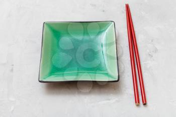 one green square saucer and red chopsticks on gray concrete board