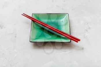 one green square saucer with red chopsticks on gray concrete surface