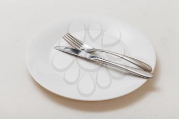 food concept - white plate with parallel knife, spoon on white plastering board