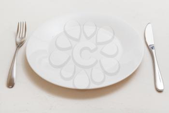 food concept - white plate with knife, spoon on white plastering board