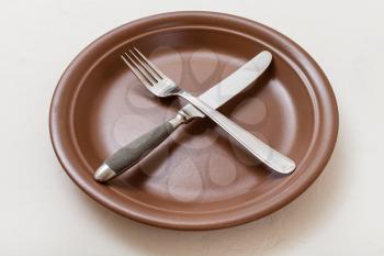 food concept - brown plate with crossing knife, spoon on white plastering board