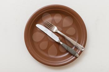 food concept - top view of brown plate with parallel knife, spoon on white plastering board