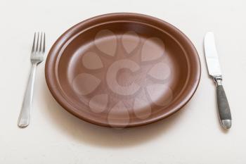 food concept - brown plate with knife, spoon on white plastering board