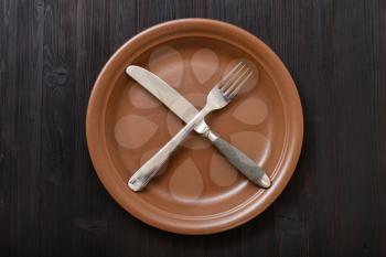 food concept - top view of brown plate with crossing knife, spoon on dark brown table
