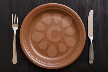 food concept - top view of brown plate with knife, spoon on dark brown table