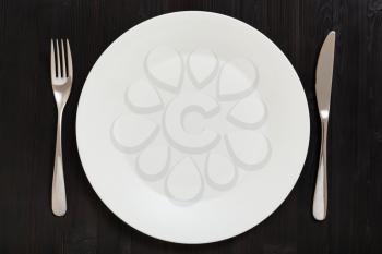 food concept - top view of white plate with knife, spoon on dark brown table
