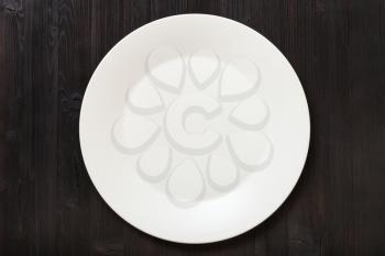 top view of one white plate on dark brown table