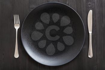 food concept - top view of black plate with knife, spoon on dark brown table