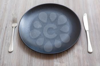 food concept - black plate with knife, spoon on gray brown table