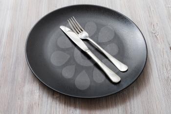 food concept - black plate with parallel knife, spoon on gray brown table