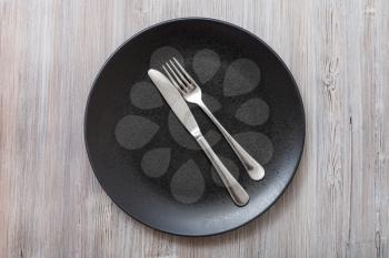 food concept - top view of black plate with parallel knife, spoon on gray brown table