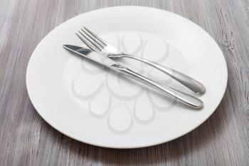 food concept - white plate with parallel knife, spoon on gray brown table