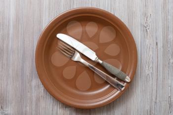 food concept - top view of brown plate with parallel knife, spoon on gray brown table
