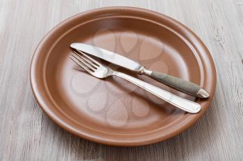 food concept - brown plate with parallel knife, spoon on gray brown table