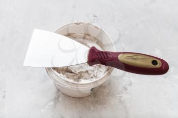 metal spatula with plastic handle on tube with putty on the concrete floor
