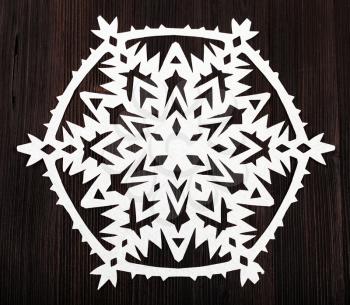 top view of snowflake carved from paper on dark brown wooden plank