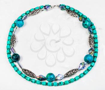 top view of round necklace from chrysocolla natural gem stone ball, artificial turquoise and abalon nacre and silver beads on concrete board