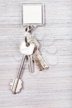 bunch of door keys with white blank key chain on wooden background