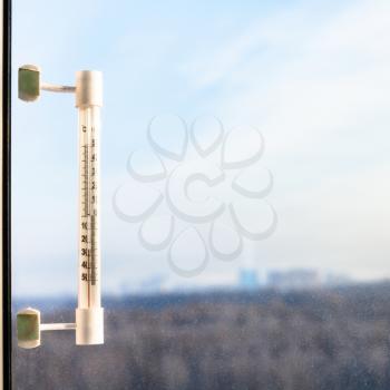 outdoor thermometer with minus 25 degrees celsius temperature on window pane in cold winter day