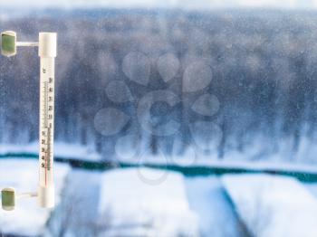 outdoor thermometer with minus 25 degrees celsius temperature on home window in cold winter day