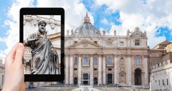 travel concept - tourist photographs St Peter statue in front of Basilica in Vatican city on tablet in Italy