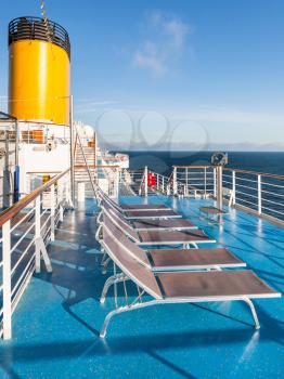 empty sunbathing chairs on upper deck of cruise liner in sunny day