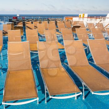 many empty sunbathing chairs on upper deck of cruise liner