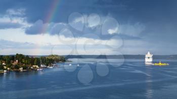 panorama with white cruise liner, village on the seacoast and dark blue rainy clouds with rainbow over Baltic Sea in sunny autumn day, Sweden