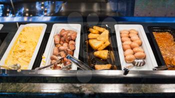 self-service buffet with meals for breakfast - bacon, scrambled eggs, fried sausages, potato naggets, boiled eggs, etc