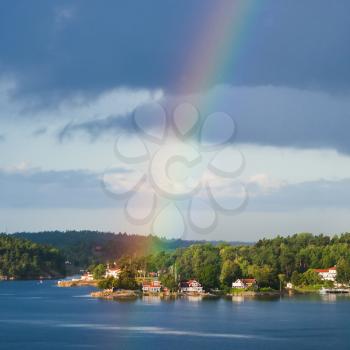 green coast of Baltic Sea with village and rainbow in blue sky in sunny autumn day, Sweden