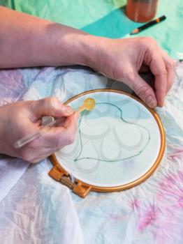 batik painting workshop - artist draws contour of heart on batik on white silk canvas clamped in the hoop