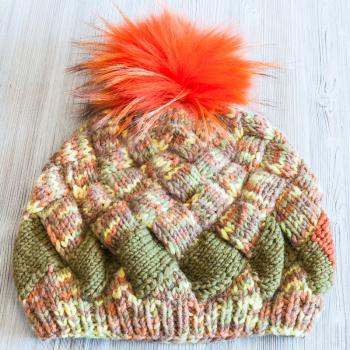hand knitted beanie with orange pompon on wooden table