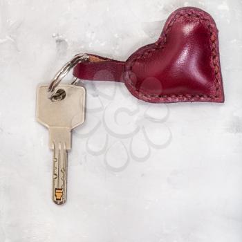 door key with red leather heart shape trinket on concrete plate