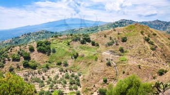 travel to Italy - panorama with green mountain slope and Etna mount near Calatabiano town in Sicily