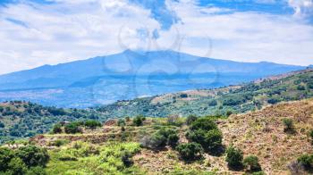 travel to Italy - panorama with green mountain slope and Etna volcano near Calatabiano town in Sicily