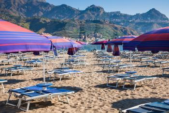 travel to Italy - Parasols and beds on urban beach in giardini naxos town in Sicily in morning