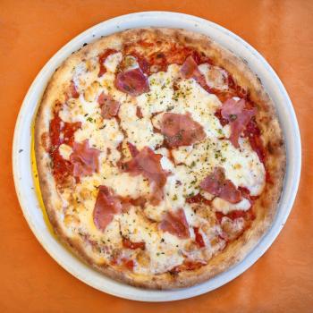 travel to Italy, italian cuisine - top view of pizza with prosciutto on plate in Sicily