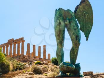 AGRIGENTO, ITALY - JUNE 29, 2011: Icarus statue and Temple of Juno in Valley of the Temples in Sicily. This area has largest and best-preserved ancient Greek buildings outside of Greece itself
