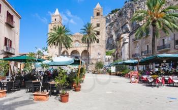 CEFALU, ITALY - JUNE 25, 2011: people in outdoor cafe near Duomo di Cefalu in Sicily. Cathedral - Basilica of Cefalu was erected in 1131 in the Norman architectural style