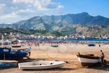 GIARDINI NAXOS, ITALY - JULY 6, 2011: people near boats on beach in Giardini Naxos in evening. Naxos was founded by Thucles the Chalcidian in 734 BC, and since 1970s it has become a seaside-resort