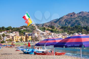 GIARDINI NAXOS, ITALY - JULY 8, 2011: flags over boats and people on urban beach of Giardini Naxos . Naxos was founded by Thucles the Chalcidian in 734 BC, and since 1970s it has become a seaside-reso