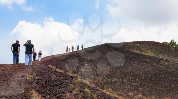 ETNA, ITALY - JULY 1, 2011 - tourists walk on ridge between old craters of Etna volcano. Mount Etna is active volcano on the east coast of Sicily, the tallest active volcano in Europe