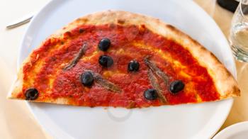 travel to Italy - above view of half of pizza with anchovies on white plate in venetian restaurant