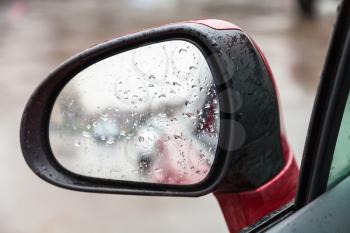 driving car in rain - raindrops on side rear view mirror in rainy day