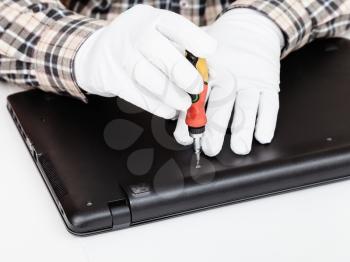 serviceman in white gloves disassembles laptop with screwdriver
