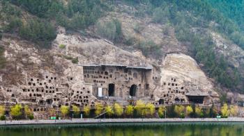 travel to China - many caves on West Hill of Chinese Buddhist monument Longmen Grottoes (Longmen Caves, Dragon's Gate) from the east bank of the Yi River in spring season
